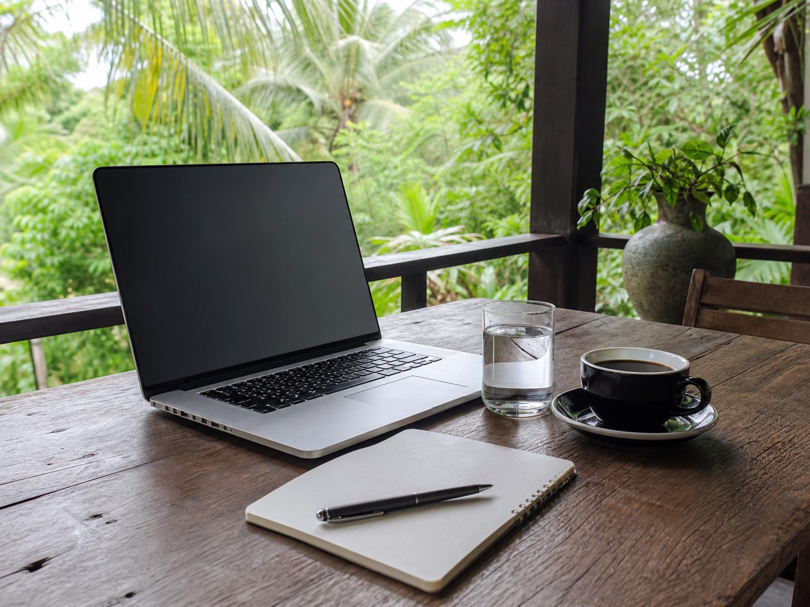 Laptop, notebook and coffee set up on a shaded terrace for a coaching call