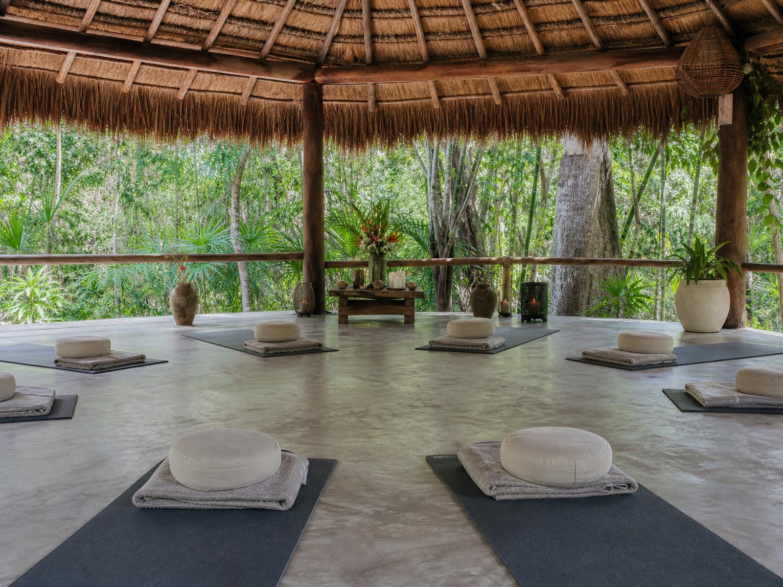 Open-air palapa retreat space in the Tulum jungle set with mats and cushions